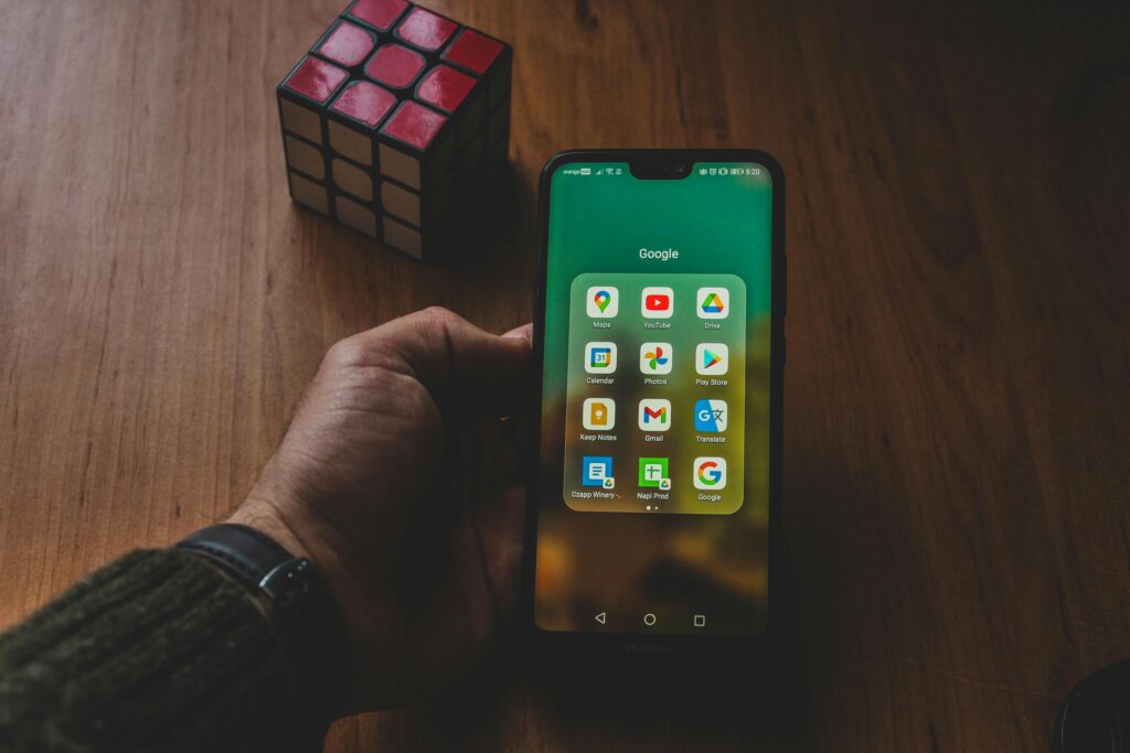 Alt Text: Digital marketing specialist holding a smartphone showing Google apps and mobile advertising tools on a desk with a Rubik's cube.