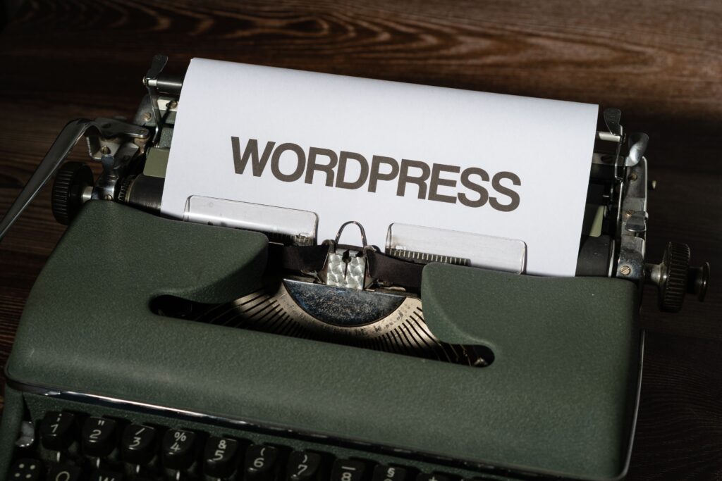 A vintage green typewriter sitting on a wooden surface, with a sheet of white paper in the carriage that reads "WORDPRESS" in bold, capitalized text.